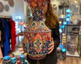 May include: A large, colorful ceramic vase with intricate floral and geometric patterns in shades of red, blue, green, and yellow. The vase has a wide, flared opening and a narrow neck.
