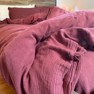 May include: A burgundy-colored, textured, waffle-weave duvet cover with a button closure. The duvet cover is on a bed with a wooden headboard.