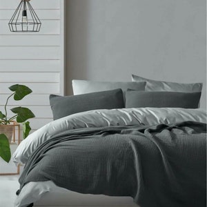 May include: A dark gray waffle weave throw blanket is draped over a bed with white bedding and gray pillows. The bed is made with a white duvet cover and a gray throw blanket.