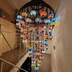 May include: A large, ornate chandelier with numerous colorful glass globes. The globes are in various shapes and sizes, featuring intricate mosaic patterns in shades of blue, red, orange, and yellow. The chandelier hangs from a dark, wrought-iron frame.