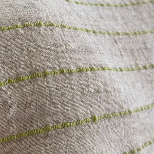 Puede incluir: Primer plano de una tela beige claro con finas rayas verdes. La tela tiene una textura tejida y un brillo sutil.