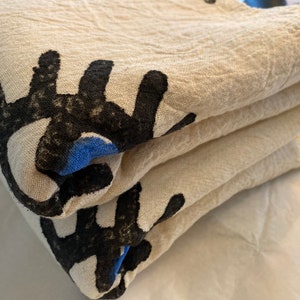 May include: A stack of folded white cotton fabric with black and blue abstract designs printed on the fabric. The fabric has a soft, textured surface.