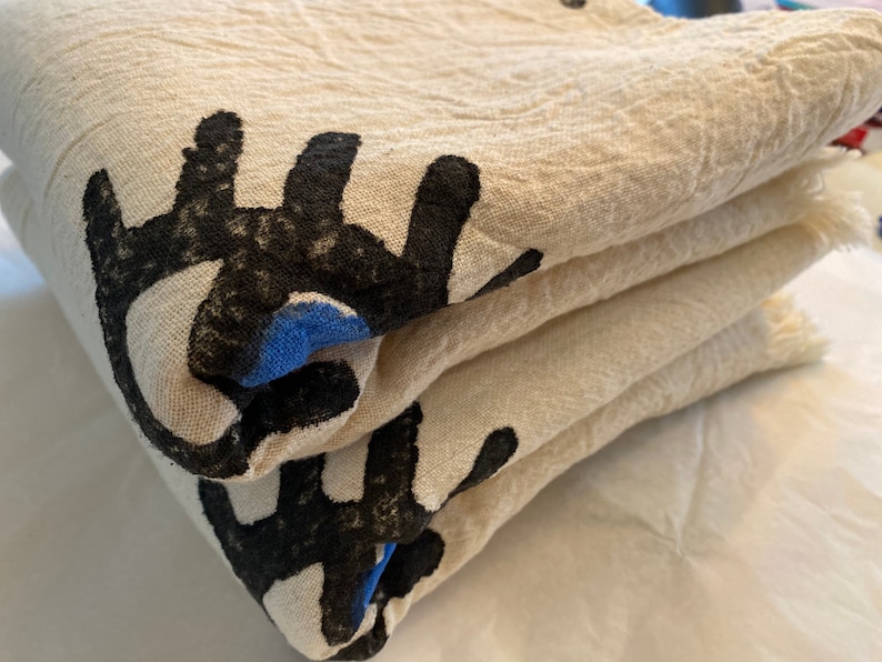 May include: A stack of folded white cotton fabric with black and blue abstract designs printed on the fabric. The fabric has a soft, textured surface.