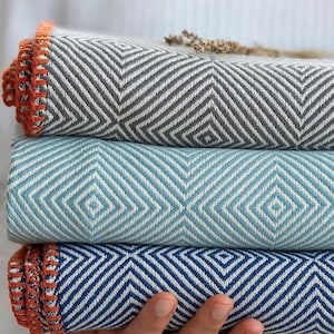 May include: Three woven blankets stacked on top of each other. The top blanket is gray with a diamond pattern, the middle blanket is light blue with a diamond pattern, and the bottom blanket is dark blue with a diamond pattern.