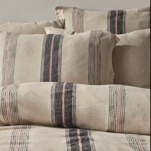 Puede incluir: Un juego de fundas de almohada a rayas en un esquema de color beige, negro y rosa. Las fundas de almohada están hechas de una tela suave y texturizada.
