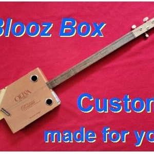 Puede incluir: Una guitarra de caja de puros hecha a medida, también conocida como "blooz box", con un cuerpo de madera y una sola cuerda. La guitarra está hecha de una caja de puros reutilizada y tiene un diseño simple.