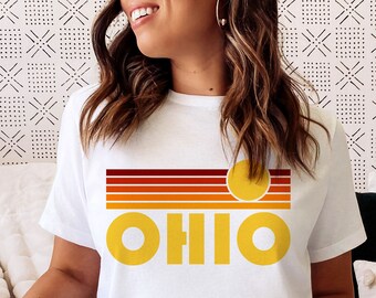 Könnte beinhalten: Weißes T-Shirt mit einem Retro-Sonnenuntergang-Motiv und dem Wort "OHIO" in gelben Buchstaben.