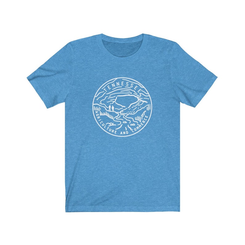 May include: A light blue t-shirt with a white graphic of the state seal of Tennessee. The seal features a mountain range, a river, and two figures standing on a hill. The text around the seal reads "Tennessee Agriculture and Commerce".