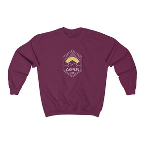 May include: Burgundy sweatshirt with a white graphic of a mountain range with a sun rising behind it. The graphic is inside a hexagon with the text "ASPEN CO" below it.