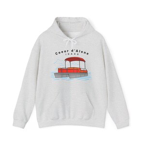 Puede incluir: Sudadera con capucha gris claro con un gráfico de un pontón rojo y gris y el texto "Coeur d'Alene Idaho". La sudadera con capucha tiene una capucha con cordón y un bolsillo delantero. El diseño está centrado en el pecho.