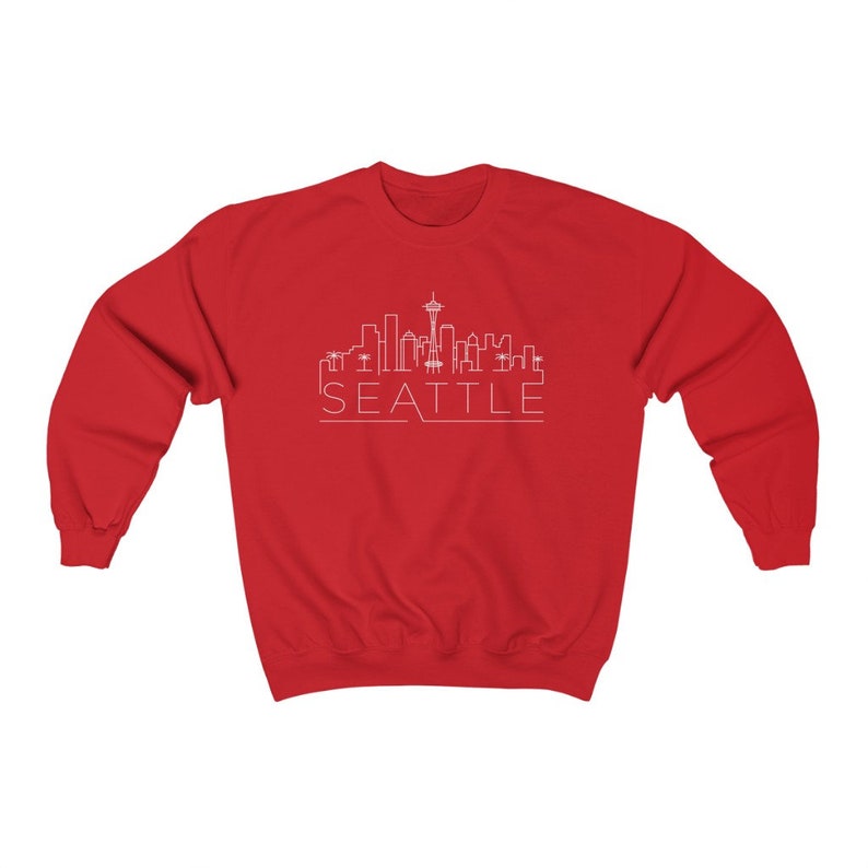 May include: Red sweatshirt with a white outline of the Seattle skyline and the word "SEATTLE" underneath.