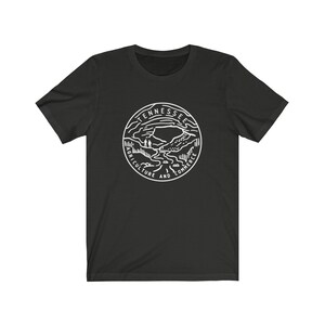 May include: Black t-shirt with a white outline of the state seal of Tennessee. The seal features a mountain range, a river, and the words "Agriculture and Commerce".
