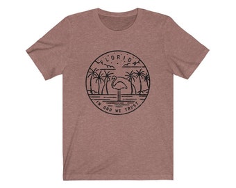 May include: A heather brown t-shirt featuring a black graphic of a flamingo standing in water with palm trees and the words "Florida In God We Trust" in a circle.