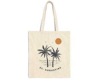 May include: A beige tote bag with a black and white illustration of two palm trees and a setting sun. The text "ST. AUGUSTINE" is printed below the palm trees.