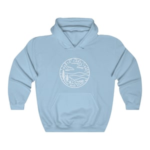 May include: Light blue hooded sweatshirt with a white outline of a circle containing the words "North Carolina" and the state motto "Esse Quam Videri" with a mountain and tree landscape inside the circle.