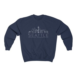 May include: Navy blue sweatshirt with a white outline of the Seattle skyline, including the Space Needle, and the word "SEATTLE" underneath.