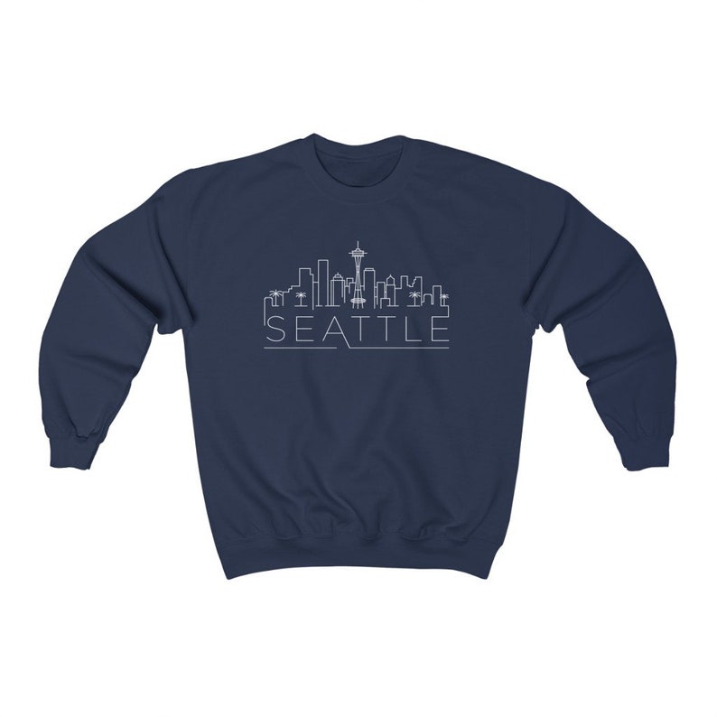 May include: Navy blue sweatshirt with a white outline of the Seattle skyline, including the Space Needle, and the word "SEATTLE" underneath.
