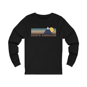 May include: Black long-sleeve t-shirt with a retro-style graphic of a mountain range, sun, and the text "NORTH CAROLINA".
