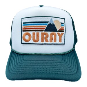May include: A white and green trucker hat with a patch featuring a mountain range, a sun, and the word "OURAY" in orange embroidery.