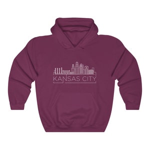 Może przedstawiać: Bordowa bluza z kapturem z białym obrysem panoramy Kansas City i napisem "KANSAS CITY" poniżej. Bluza ma przednią kieszeń i kaptur.
