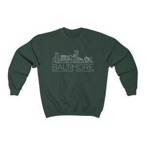 May include: A dark green sweatshirt with a white outline of the Baltimore skyline and the word "BALTIMORE" underneath.