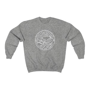 May include: A gray sweatshirt with a white outline of the state of Tennessee seal. The seal features a mountain range, a river, and the words "Agriculture and Commerce".