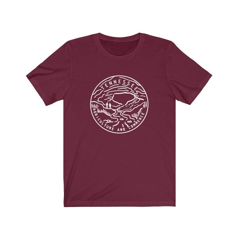 May include: A maroon t-shirt with a white graphic of the state seal of Tennessee. The seal features a mountain range, a river, and the words "Tennessee, Agriculture and Commerce".