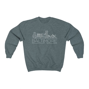May include: A dark heather grey sweatshirt with a white outline of the Baltimore skyline and the word "BALTIMORE" printed below it.