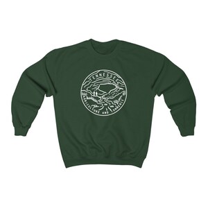 May include: A dark green sweatshirt with a white outline of the state of Tennessee seal. The seal features a mountain range, a river, and the words "Agriculture and Commerce".