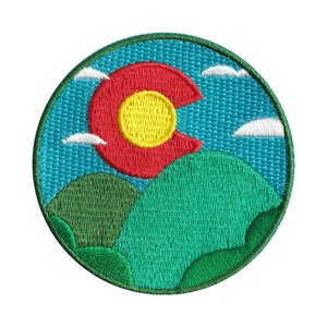 May include: Embroidered patch featuring a stylized depiction of the Colorado state flag, with a red 'C' and yellow sun, set against a blue sky with white clouds and green hills.