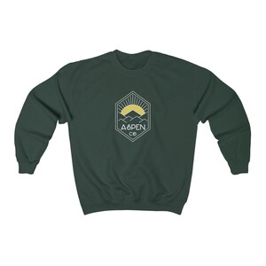May include: A dark green sweatshirt with a white logo featuring a mountain range and a sun with the text "ASPEN CO" in a hexagon.