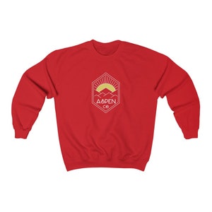 May include: Red sweatshirt with a white graphic of a mountain range with a sun rising behind it. The graphic is inside a hexagon with the text "ASPEN CO" below it.