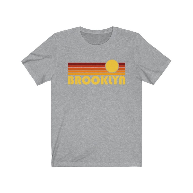 May include: A heather grey t-shirt with a retro sunset graphic and the word "BROOKLYN" in yellow.