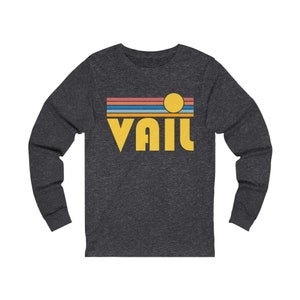 May include: A dark heather grey long-sleeve shirt with a retro-style graphic of a sunset and the word "Vail" in yellow.