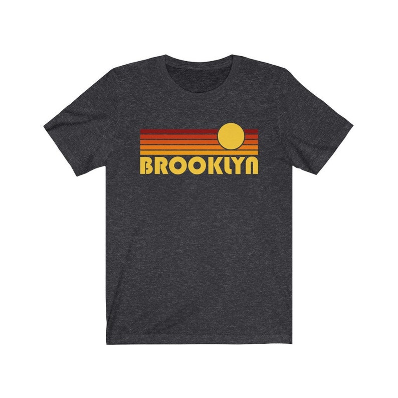 May include: A dark heather grey t-shirt with a retro sunset graphic and the word "BROOKLYN" in yellow letters.