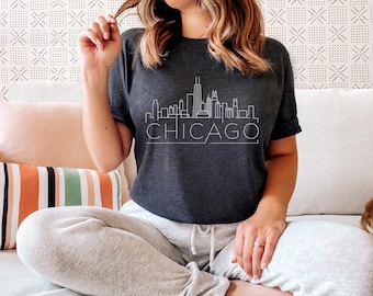 Puede incluir: Una camiseta gris oscuro con un contorno blanco del horizonte de Chicago y la palabra "CHICAGO" debajo.