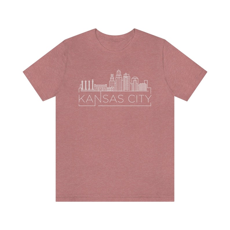 May include: A heather rose colored t-shirt with a white outline of the Kansas City skyline and the text "KANSAS CITY" in a white box.