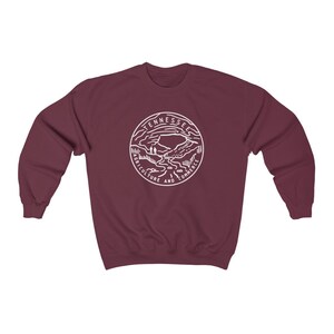 May include: Burgundy sweatshirt with a white outline of the state of Tennessee seal. The seal features a mountain range, a river, and the words "Agriculture and Commerce".