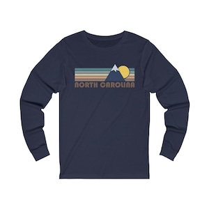 May include: A navy blue long-sleeved t-shirt with a retro-style graphic of a mountain range, a sun, and the text "NORTH CAROLINA".
