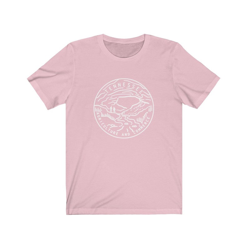 May include: A pink t-shirt with a white graphic of the state seal of Tennessee. The seal features a mountain landscape with a river flowing through it. The text "Tennessee Agriculture and Commerce" is inscribed around the seal.