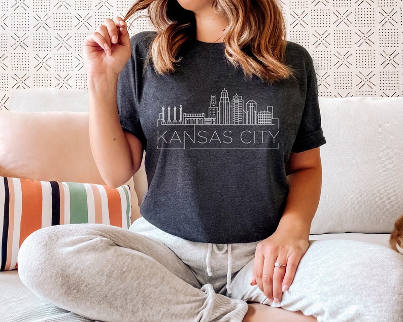 May include: A dark gray t-shirt with a white outline of the Kansas City skyline and the text "KANSAS CITY".