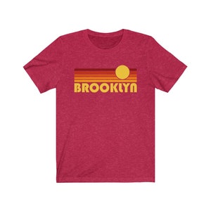 May include: A red heather t-shirt with a retro sunset graphic and the word "BROOKLYN" in yellow text.