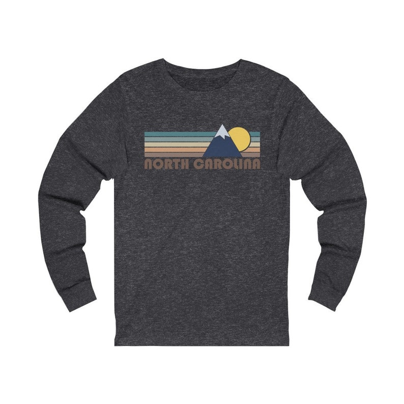 May include: A dark heather grey long-sleeve t-shirt with a retro-style graphic of a mountain range, sun, and the text "NORTH CAROLINA".