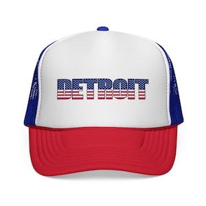 Pode incluir: Um boné de caminhoneiro vermelho, branco e azul com a palavra "DETROIT" na frente. O texto é projetado com a bandeira americana. O boné tem um painel frontal branco, uma aba vermelha e uma parte traseira de malha azul.