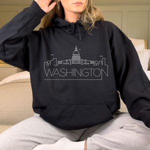 May include: Black hoodie with a white outline of the Washington D.C. skyline, including the Capitol Building, and the text "WASHINGTON" below.