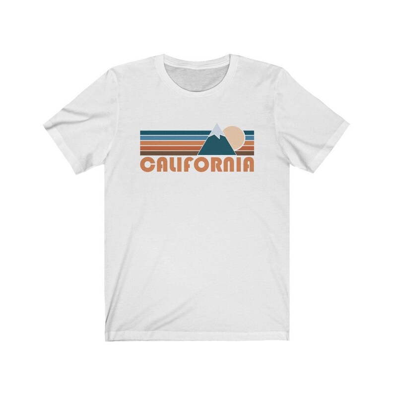 May include: White t-shirt with a retro-style graphic of a mountain range, sun, and the word "CALIFORNIA" in orange.
