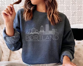 May include: A dark blue sweatshirt featuring a white outline of the Portland skyline with the word "PORTLAND" underneath.