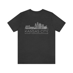 May include: A dark grey t-shirt with a white outline of the Kansas City skyline and the text "KANSAS CITY" underneath.