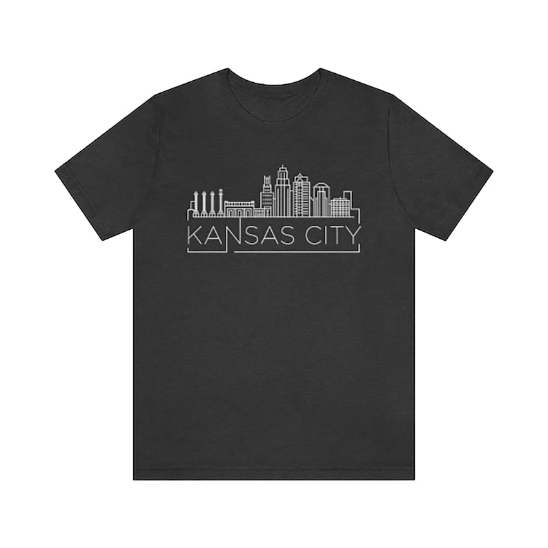 May include: A dark grey t-shirt with a white outline of the Kansas City skyline and the text "KANSAS CITY" underneath.