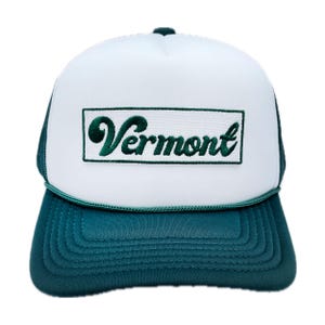 May include: White trucker hat with a green embroidered patch that says "Vermont" on the front. The hat has a dark green brim.